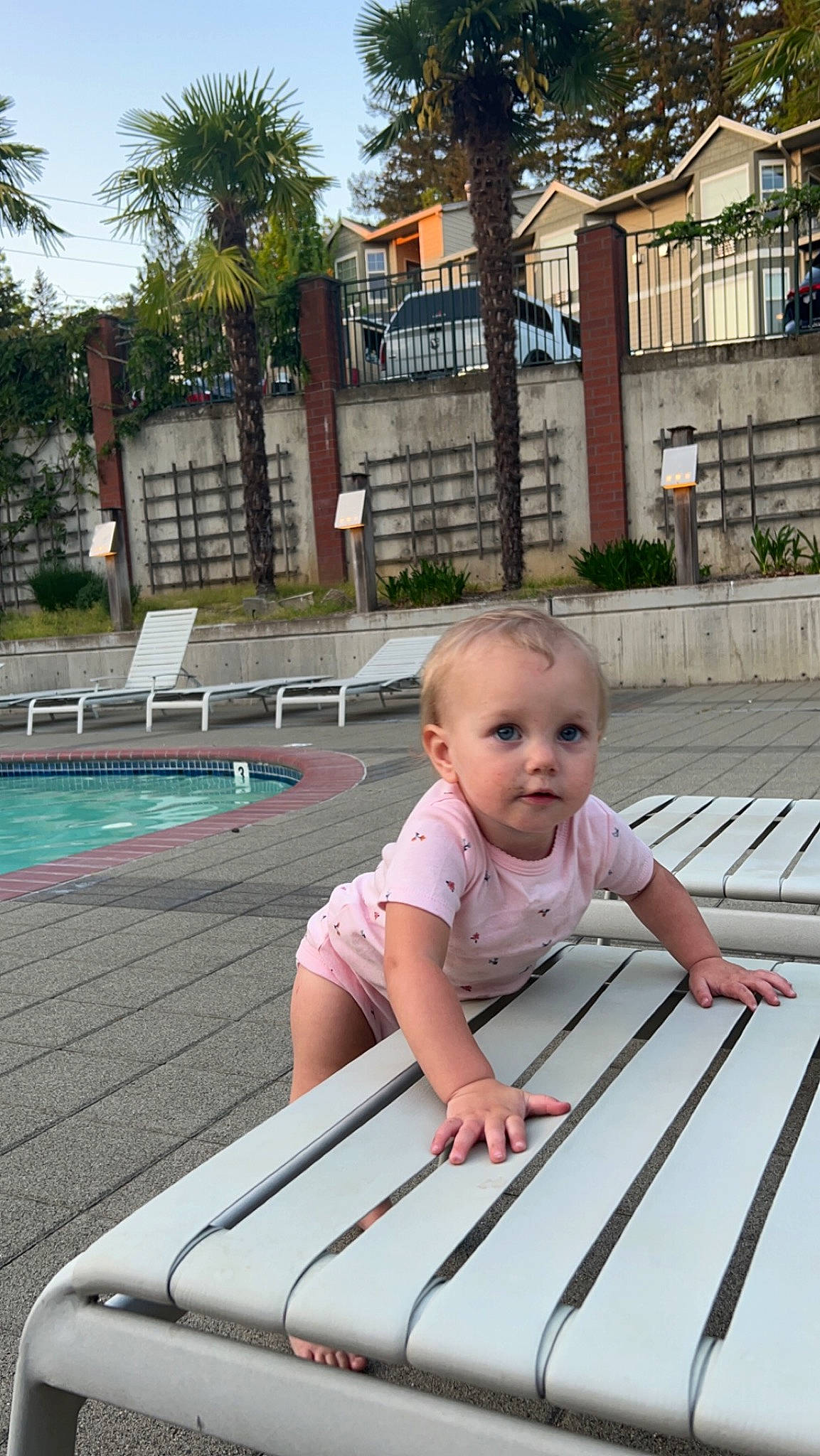 Layla is registered to the contest to win money with this photo: baby, baby_toddler_clothing, building, child, composite_material, fun, grass, leisure, outdoor_furniture, palm_tree, person, plant, recreation, sitting, sky, sleeve, swimming_pool, toddler, tree, water