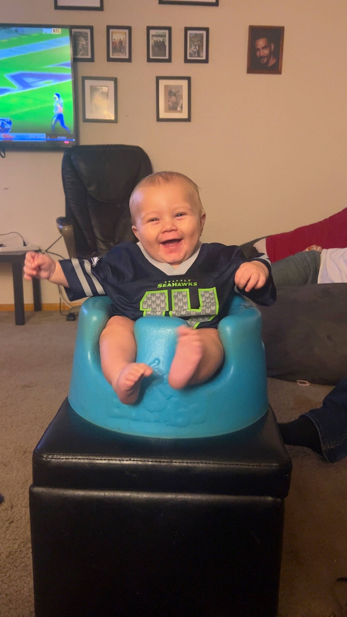 Shannon is registered to the contest to win money with this photo: baby, baby_toddler_clothing, chair, child, comfort, couch, display_device, electric_blue, flooring, fun, green, lap, led_backlit_lcd_display, person, picture_frame, play, room, sitting, smile, television