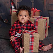 Kalea is registered to the contest to win money with this photo: baby, child, plaid_pajamas, gift_box, holiday, christmas, nutcracker, books, red_and_black, wrapped_gifts, indoors, floor, sitting, curly_hair, cute, decor, festive, portrait, smiling, barefoot