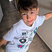 Louka participe au concours pour gagner de l'argent avec cette photo : boy, cartoon_print, casual_clothing, child, floor_tiles, hallway, happy, home_interior, indoor, light_skin, mismatched_socks, necklace, patterned_wallpaper, playful, portrait, short_hair, shorts, smiling, standing, white_tshirt