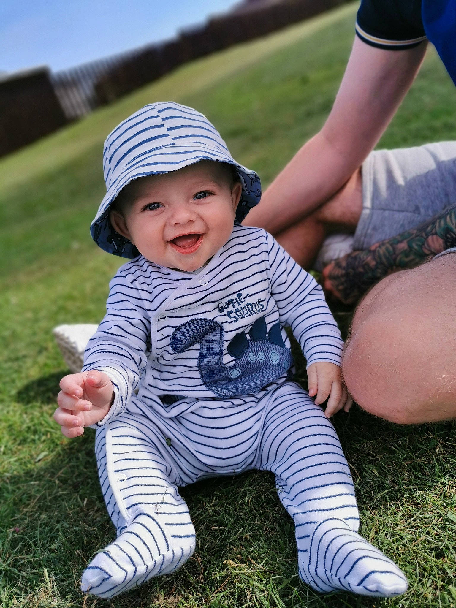 Lyle is registered to the contest to win money with this photo: baby, child, finger, grass, hat, headgear, headwear, joy, leg, person, plant, play, sitting, skin, toddler, vacation