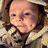 baby, infant, child, portrait, smiling, dimple, face, eyes, hand, blanket, bundled, cozy, indoor, warm, close_up, sitting, candid, patterned_fabric, soft_lighting, home