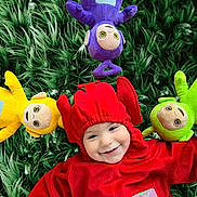 Kamil participe au concours pour gagner de l'argent avec cette photo : baby, child, infant, red_costume, plush_toy, teletubby, stuffed_animal, grass, green_background, smile, portrait, lying_down, colorful, toys, purple_plush, yellow_plush, green_plush, happy, closeup, fabric_texture