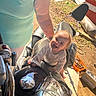 Damon is registered to the contest to win money with this photo: baby, box, child, clothing, dirt, foot, grass, hand, happy, metal, motorcycle, outdoor, person, seat, shadow, smiling, sunlight, tank_top, tattoo, tools