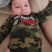 Jose is registered to the contest to win money with this photo: baby, blanket, camouflage, child, clothing, couch, cute, face, happy, head, indoor, infant, lying_down, onesie, person, portrait, skin, smile, soft_texture, young
