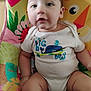 Jose joined the competition — help win amazing prizes! baby, child, onesie, colorful_cushion, pattern, sitting, infant, cute, soft_fabric, indoor, person, young_child, clothing, skin, face, head, legs, arm, text_on_clothing, blurred
