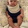 baby, infant, child, pillow, animal_print, bib, navy_blue_clothing, sitting, blanket, bed, cute, indoor, portrait, face, feet, hand, expression, comfort, soft, home