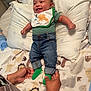 baby, smiling, infant, clothing, green_socks, jeans, striped_shirt, bib, hands, bed, pillow, blanket, animal_print, face, person, indoor, happy, cute, cozy, family