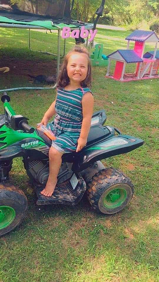 Paisley is registered to the contest to win money with this photo: automotive_tire, automotive_wheel_system, bumper, fender, fun, grass, green, joy, motor_vehicle, person, pink, recreation, riding_toy, shorts, smile, t_shirt, tire, toddler, tread, tree