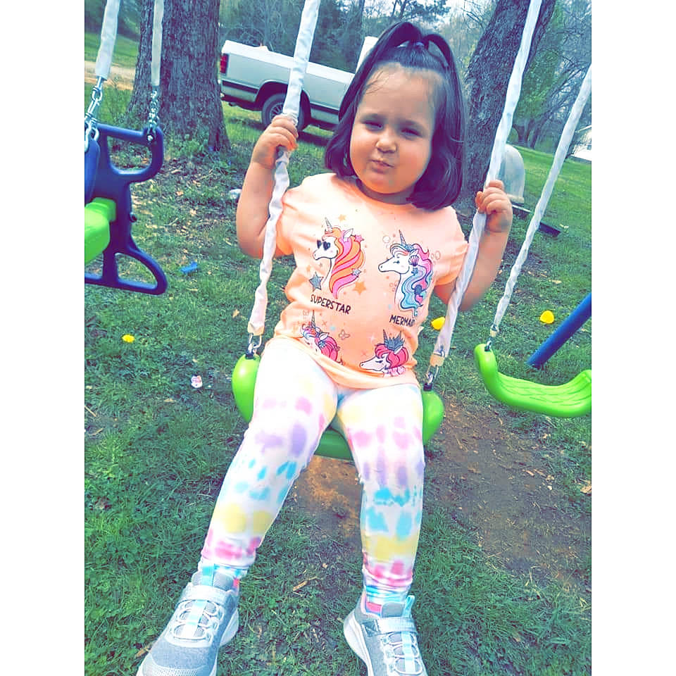 Paisley is registered to the contest to win money with this photo: child, cool, face, fun, grass, happy, human_leg, knee, leisure, magenta, pattern, person, plant, play, recreation, shoe, sitting, thigh, tire, toddler