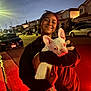 person, dog, french_bulldog, street, night, smiling, holding, hoodie, car, sidewalk, residential_area, outdoor, pet, happy, urban, canine, evening, headwear, glasses, joy