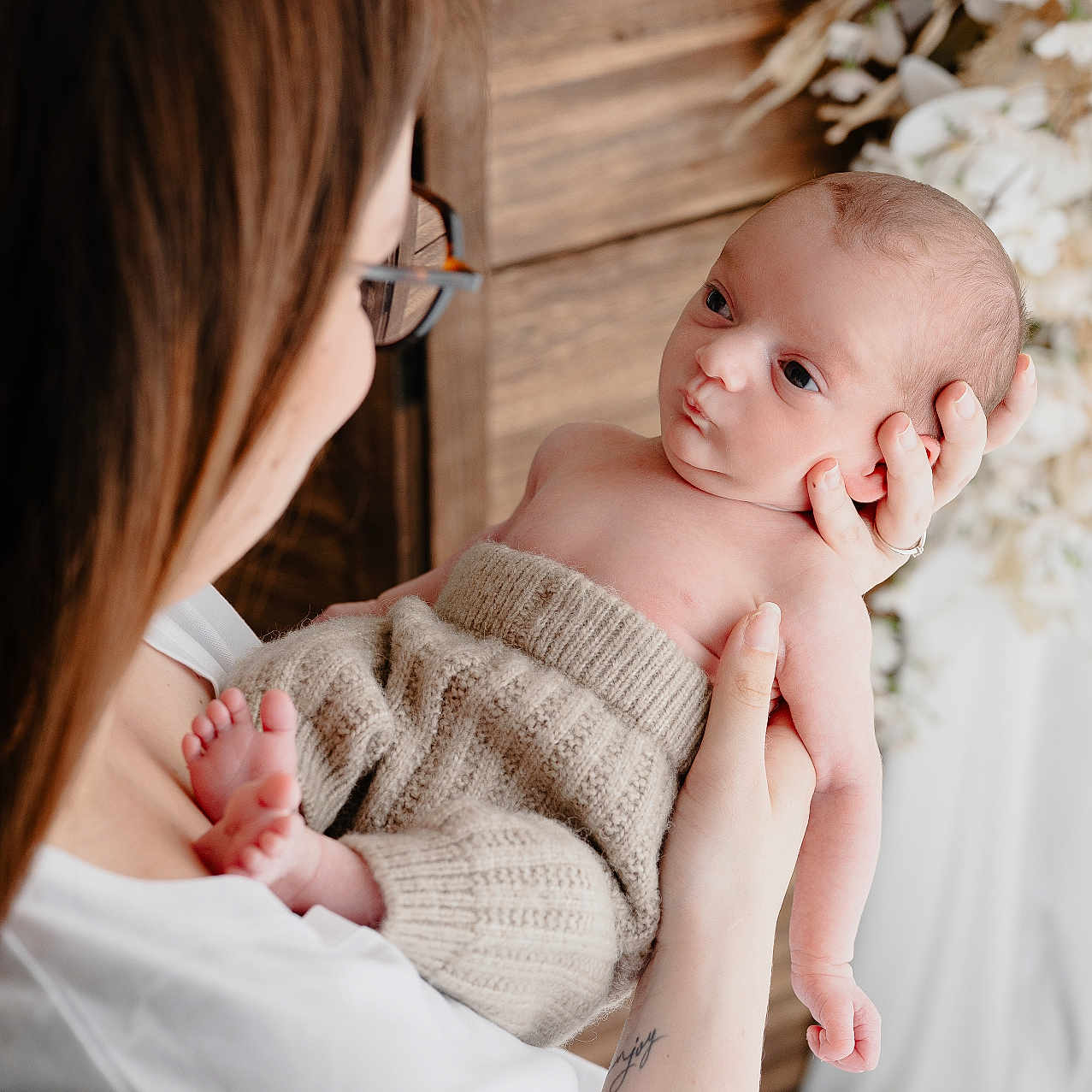 Jules participe au concours pour gagner de l'argent avec cette photo : baby, expression, face, family, glasses, holding, indoor, infant, knit_pants, mother, newborn, parenting, person, portrait, skin, soft_light, tattoo, white_clothing, woman, wooden_background