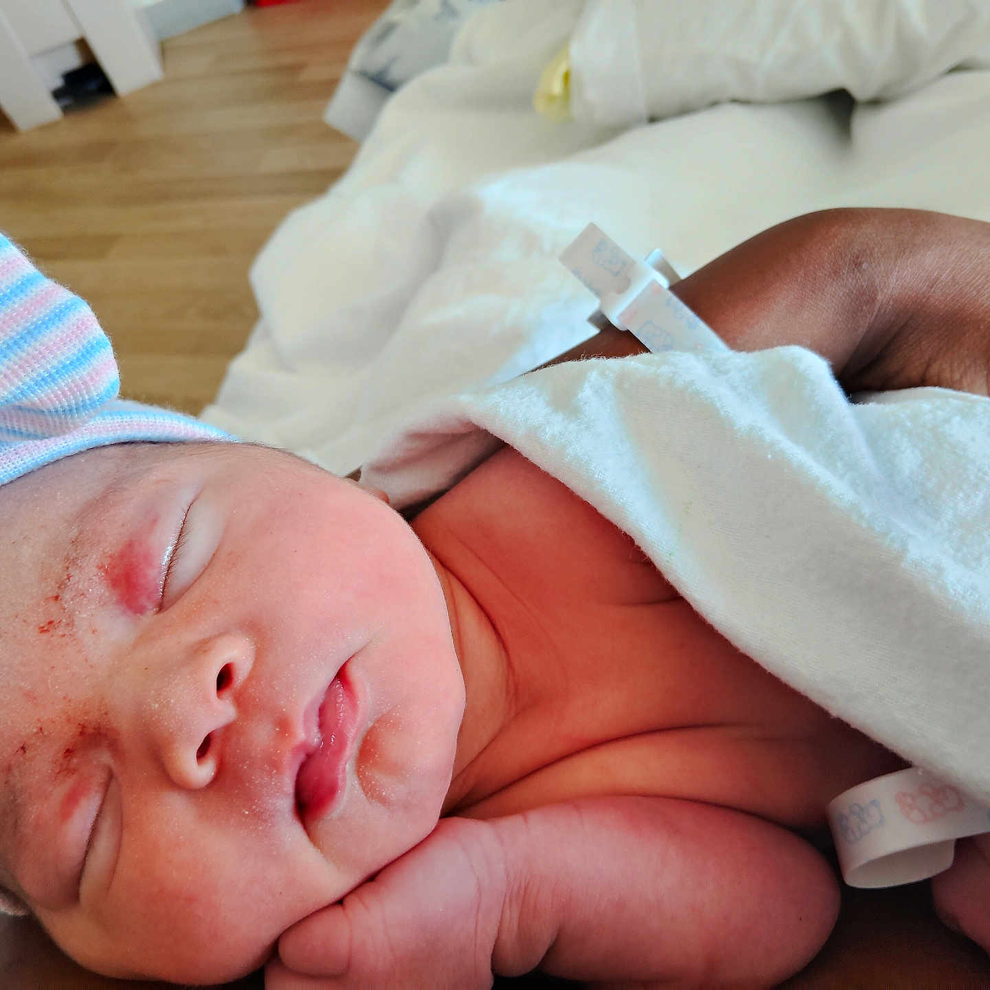 Xamira is registered to the contest to win money with this photo: adult_hand, baby, blanket, child, closeup, face, hand, hat, hospital, indoors, infant, newborn, peaceful, person, portrait, resting, skin, sleeping, soft_light, striped_hat