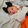 baby, newborn, headband, black_bow, white_clothing, orange_tulle, bed, blanket, soft, face, infant, cute, laying, indoors, portrait, child, small_hand, sleepwear, cozy, resting