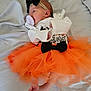 baby, infant, tutu, orange, black_bow, pacifier, bed, blanket, clothing, cute, newborn, person, lying_down, headband, foot, sleepwear, soft, indoors, celebration, resting