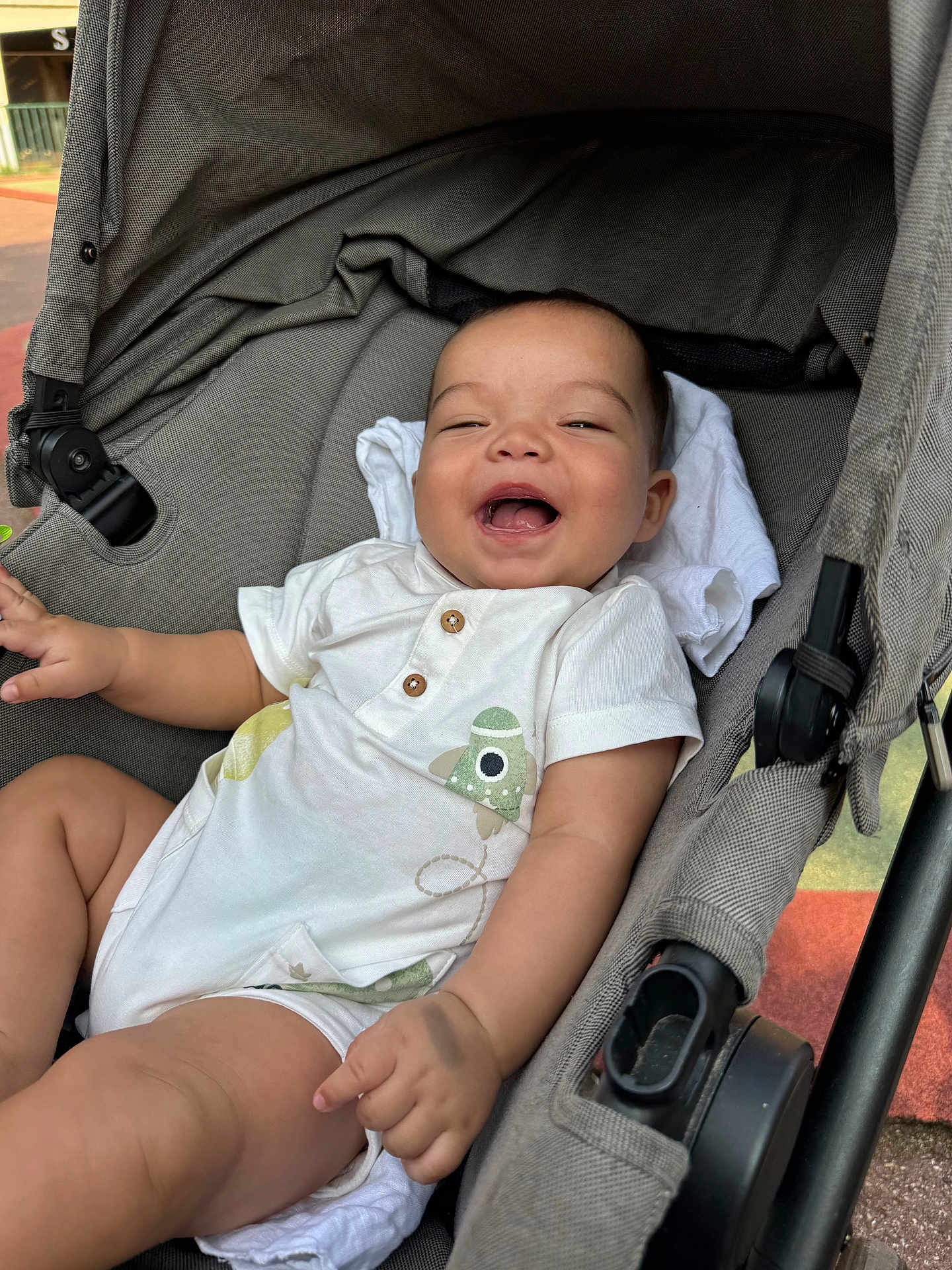 Thiago participe au concours pour gagner de l'argent avec cette photo : baby, child, stroller, smiling, laughing, onesie, white_clothing, infant, seat, fabric, cute, happy, outdoor, person, portrait, hand, leg, head, baby_clothes, comfort