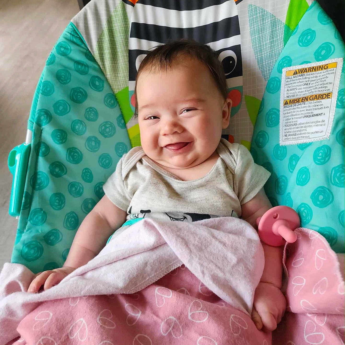 Zoey is registered to the contest to win money with this photo: baby, baby_seat, blanket, child, clothing, comfort, cute, face, happy, head, indoor, infant, pacifier, person, pink_blanket, playful, relaxed, seat, smiling, zebra_pattern