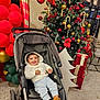 baby, child, stroller, christmas_tree, christmas_decorations, presents, balloons, holiday, smiling, cute, indoor, festive, red, green, gold, shoes, hoodie, portrait, floor, decor