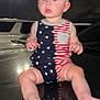 Bentley is registered to the contest to win money with this photo: baby, child, infant, stars_and_stripes, romper, night, outdoor, car, street_lamp, reflection, barefoot, blue_eyes, light_glow, portrait, sitting, head, face, skin, hand, foot