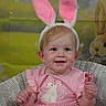 Paige is registered to the contest to win money with this photo: baby, child, pink_dress, bunny_ears, wicker_chair, smiling, cute, indoor, portrait, costume, easter, plush_toy, headband, pastel_background, happy, infant, sitting, face, person, young_child