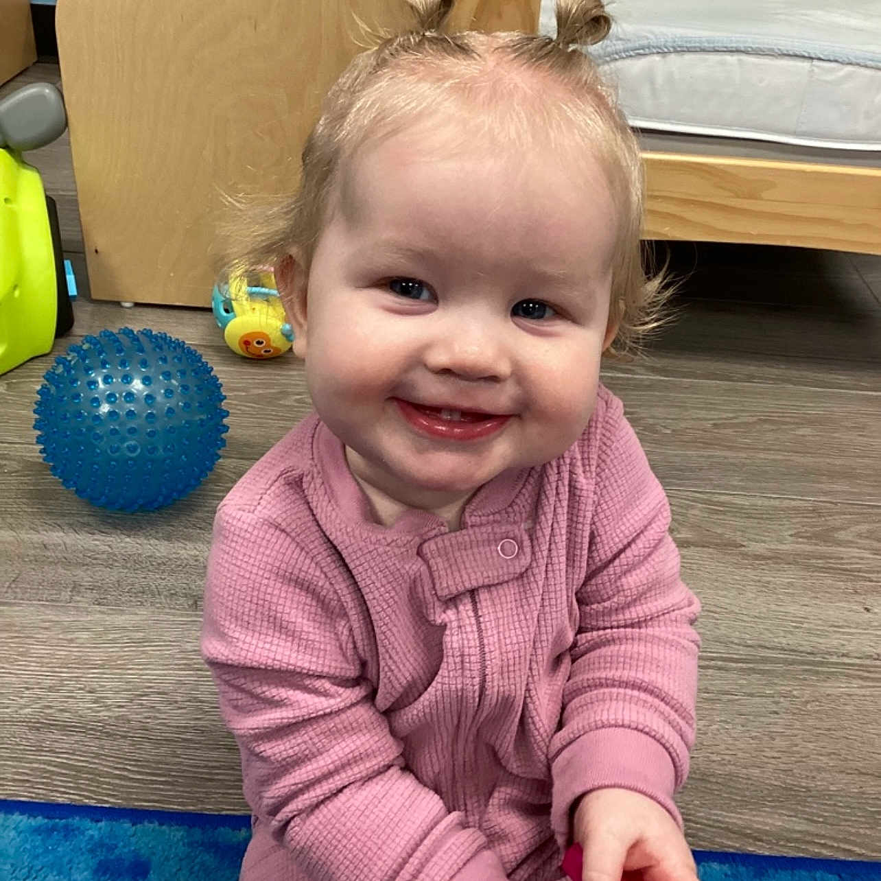 Paige joined the competition — help win amazing prizes! toddler, child, smiling, pink_clothing, toy, playroom, blue_ball, wooden_bed, flooring, hair_tied, happy, indoor, person, candid, cute, young_child, baby, floor_mat, playful, portrait
