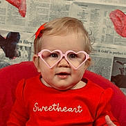Paige joined the competition — help win amazing prizes! toddler, child, glasses, heart_shaped_glasses, red_sweater, sweetheart_text, newspaper_background, decorative_hearts, red_hair_clip, indoor, portrait, cute, smiling, baby, seat, pink, red, face, hand, fashion