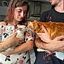 cat, person, indoor, kitchen, holding, pet, cute, feline, orange_cat, white_cat, floral_clothing, tattoo, smile, interaction, face, arm, hand, young_adult, casual, domestic