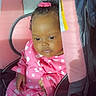 baby, infant, child, pink_clothing, polka_dot, car_seat, seat_belt, bow, hair_accessory, cute, portrait, indoors, sitting, soft_light, skin, face, hands, young_child, comfort, relaxed