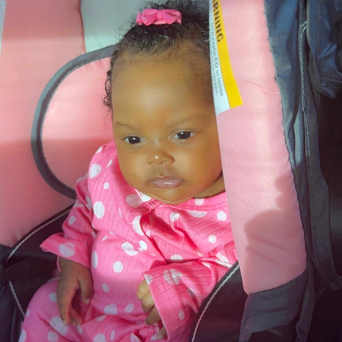 Symphony joined the competition — help win amazing prizes! baby, infant, child, pink_clothing, polka_dot, car_seat, seat_belt, bow, hair_accessory, cute, portrait, indoors, sitting, soft_light, skin, face, hands, young_child, comfort, relaxed