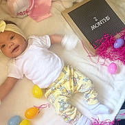 Briella is registered to the contest to win money with this photo: baby, infant, 2_months, smiling, headband, white_shirt, yellow_pants, stuffed_animals, easter_eggs, pink_shredded_paper, blanket, toy, hand, soft_toys, lying_down, cute, indoors, celebration, child, happy