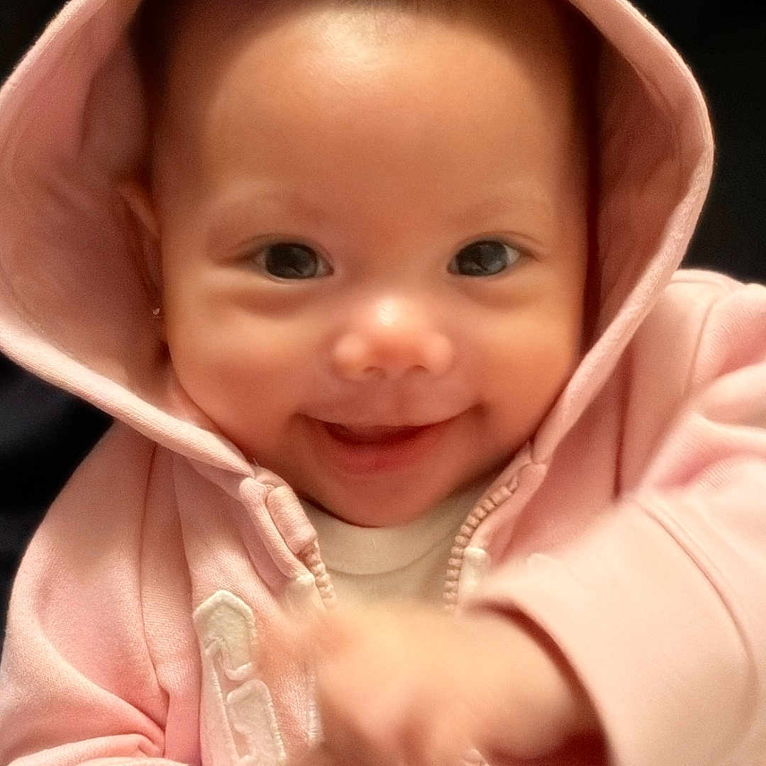 Briella is registered to the contest to win money with this photo: baby, child, hoodie, pink_clothing, smile, face, eyes, cute, happy, infant, portrait, baby_clothes, hood, ears, gesture, warm_clothing, young_child, indoor, closeup, person