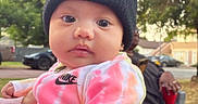 Briella is registered to the contest to win money with this photo: baby, child, hat, knit_hat, tie_dye, nike, jacket, outdoor, park, trees, person, hand, holding, red_cup, adult, curious, face, eyes, clothing, daytime