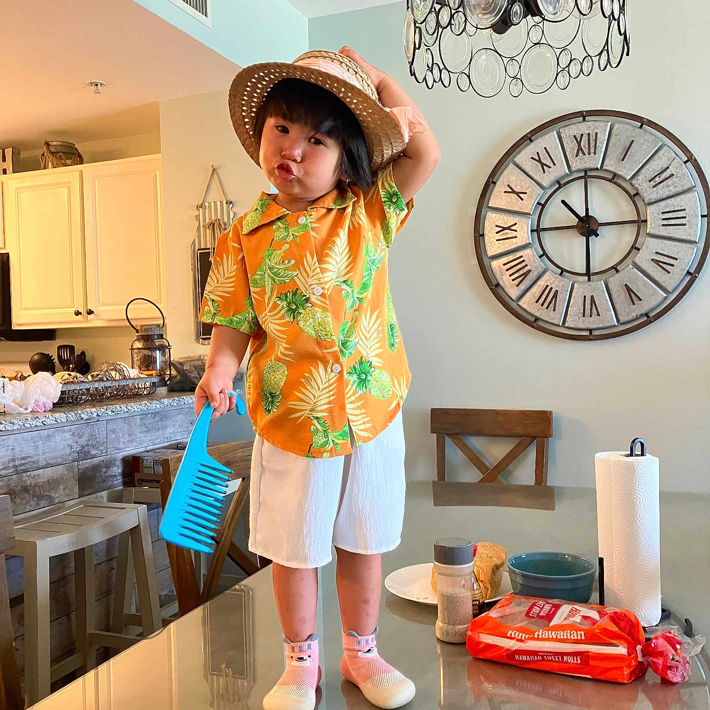 Tesla Lam Tran is registered to the contest to win money with this photo: bread, chair, chandelier, child, clock, comb, counter, cup, food, glass_table, hat, kitchen, orange_shirt, paper_towel, person, pink_socks, playful, shoes, table, white_shorts