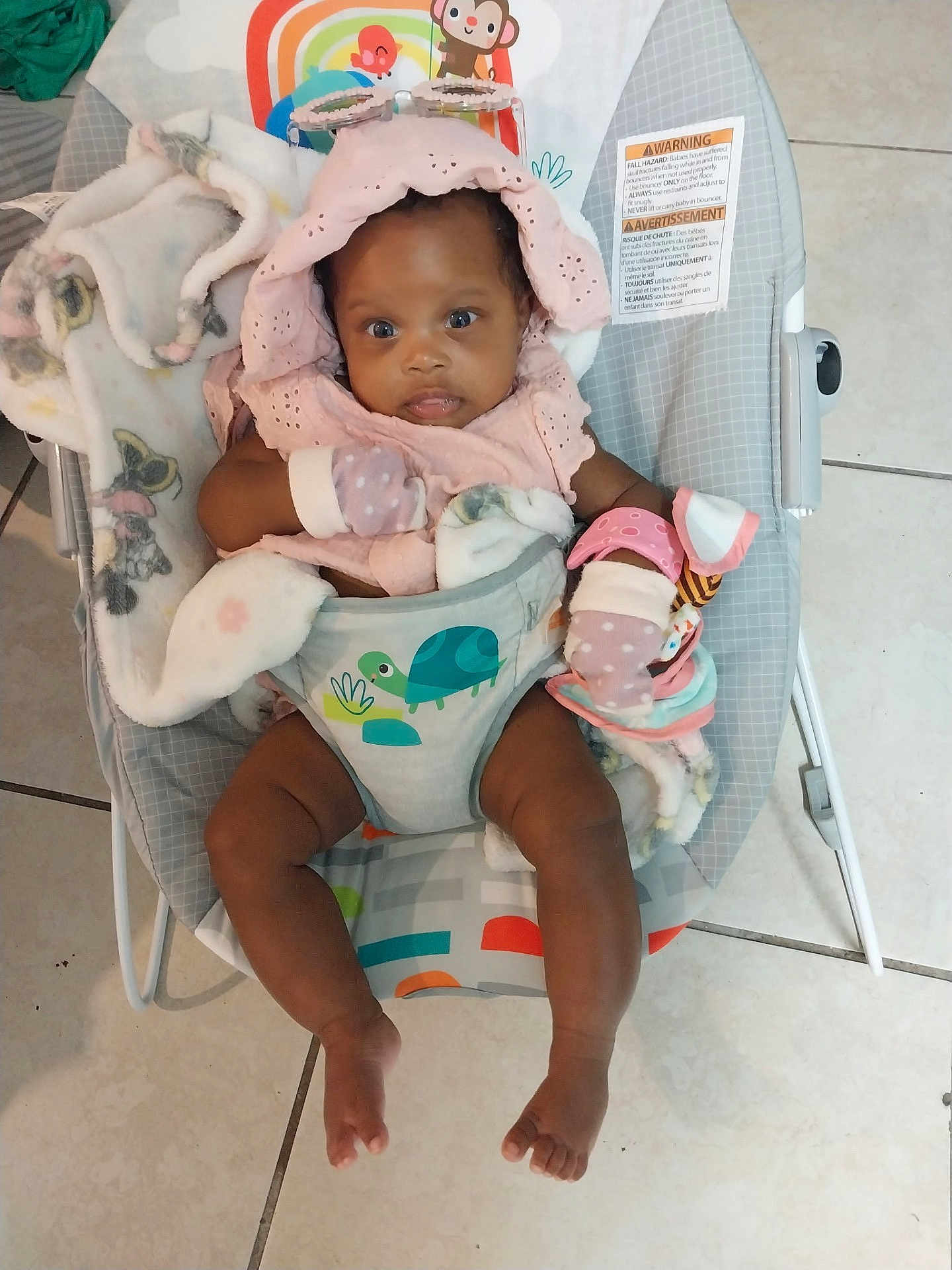 Journey is registered to the contest to win money with this photo: baby, infant, bouncer, blanket, pink_clothing, mittens, toy, floor_tiles, baby_seat, child, cute, indoor, toddler, colorful, animal_print, comfort, portrait, smiling, happy, seated