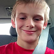 Wyatt is registered to the contest to win money with this photo: child, boy, smile, red_shirt, seatbelt, car, interior, head, face, young, casual, portrait, happy, person, sitting, vehicle, seat, window, daylight, hair