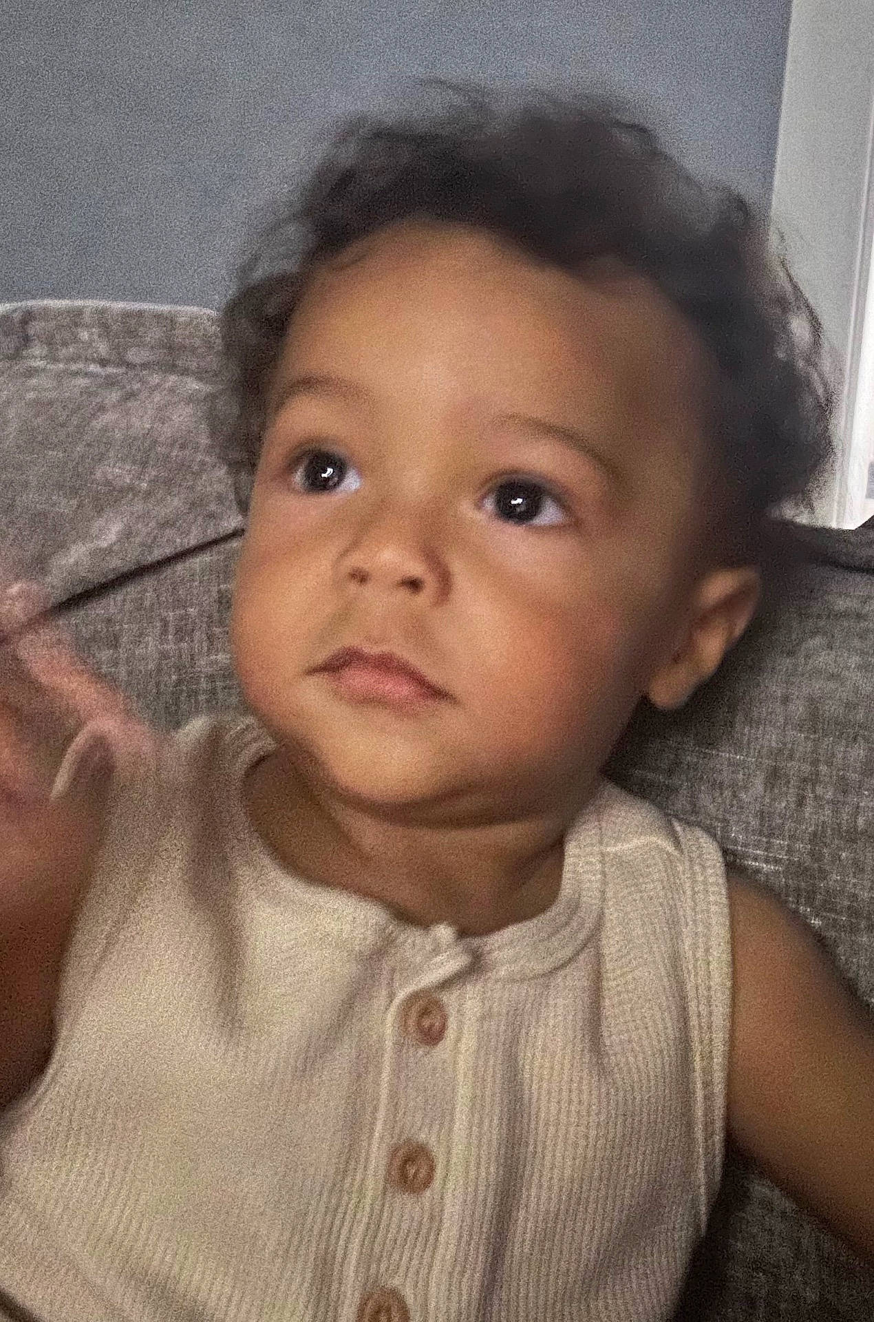 blur, buttoned_shirt, casual, child, clothing, couch, curly_hair, expression, eyes, face, furniture, hand, indoor, person, portrait, seated, skin, sleeveless, toddler, young