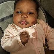 Sage is registered to the contest to win money with this photo: baby, cheeks, child, closeup, clothing, cute, expression, eyes, face, hand, indoor, infant, lying_down, newborn, person, pink_outfit, portrait, skin, sleeping_bag, soft_texture