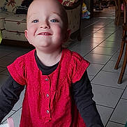 Lysis a rejoint le concours — aidez-le/la à gagner de superbes lots ! toddler, child, smiling, indoor, red_dress, black_shirt, blue_eyes, happy, face, person, floor_tiles, couch, floral_pattern, furniture, toy, clown_toy, home, portrait, long_sleeve, bright