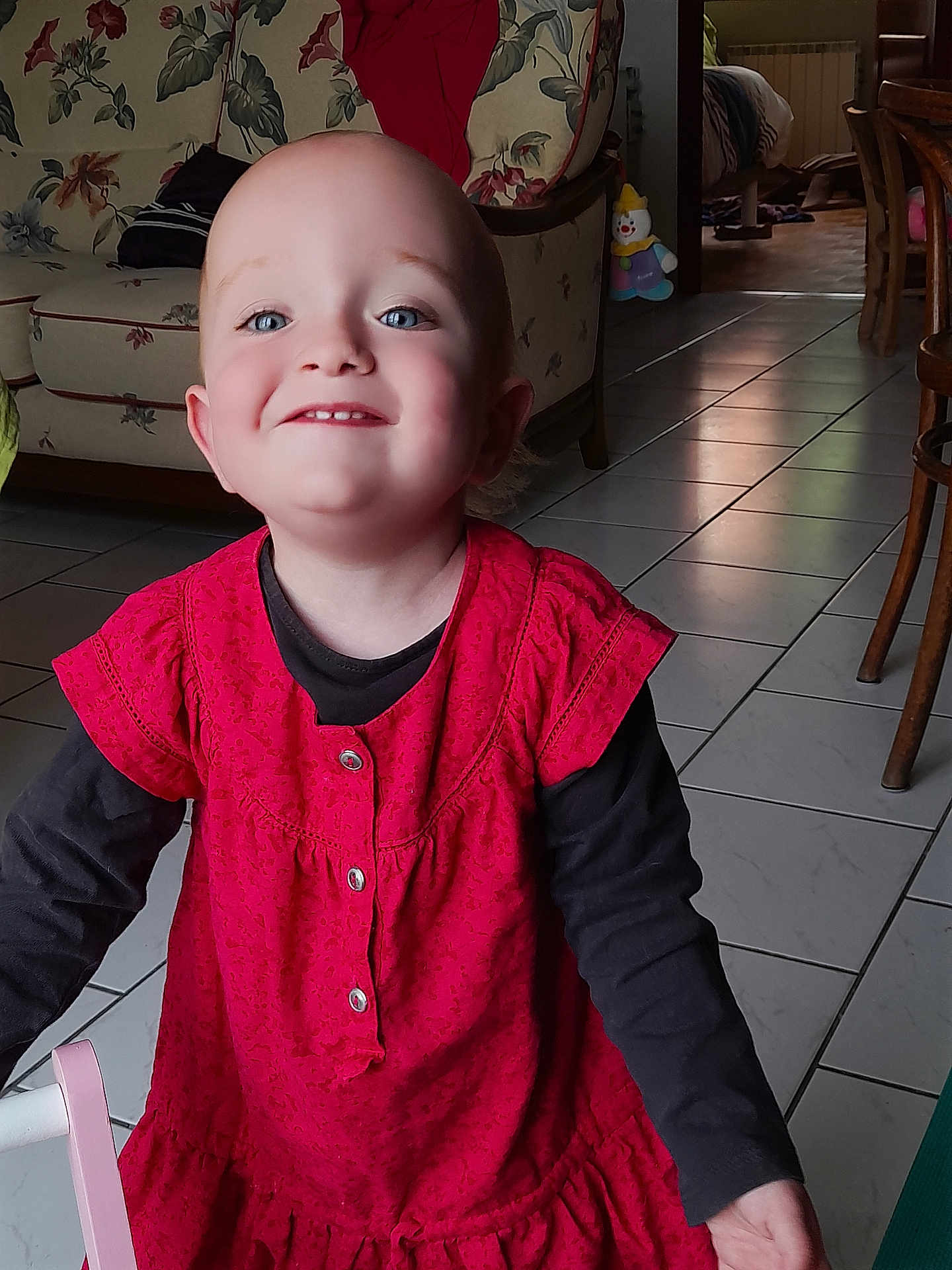 Lysis a rejoint le concours — aidez-le/la à gagner de superbes lots ! toddler, child, smiling, indoor, red_dress, black_shirt, blue_eyes, happy, face, person, floor_tiles, couch, floral_pattern, furniture, toy, clown_toy, home, portrait, long_sleeve, bright