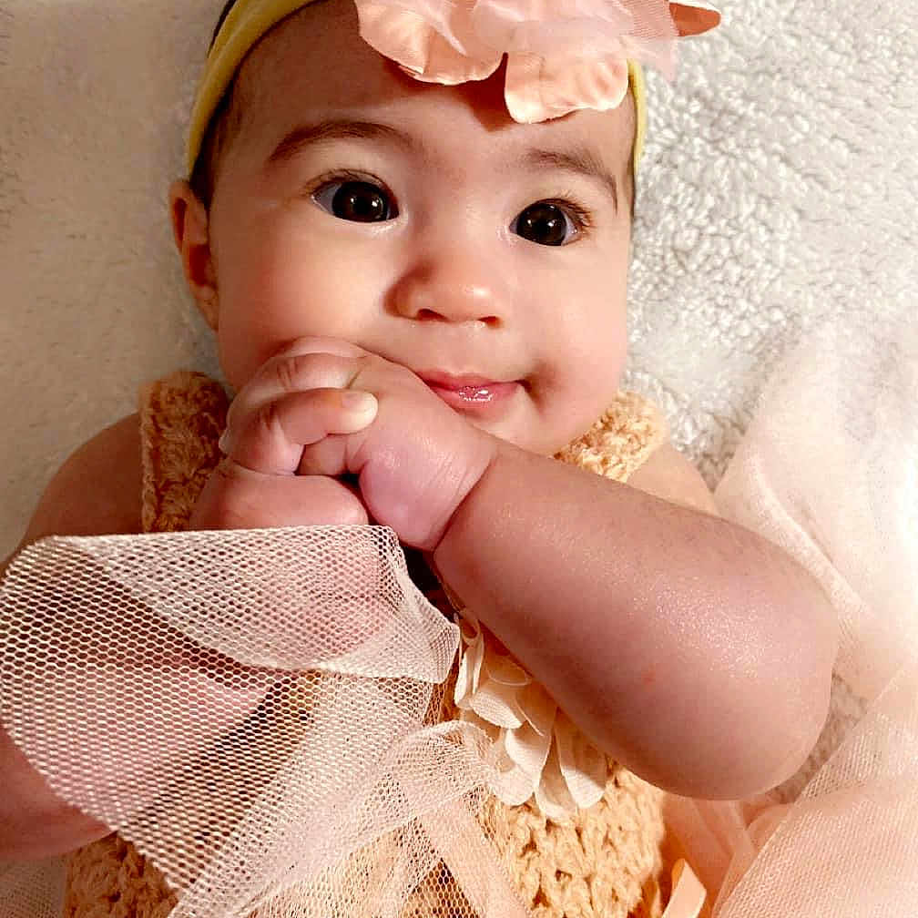 Azaylie is registered to the contest to win money with this photo: accessories, baby, biting, bodypart, bonnet, clothing, face, finger, flower, happy, hat, head, headband, person, petal, photography, plant, portrait, sleeve, smile