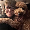 Toby Broadwater joined the competition — help win amazing prizes! woman, person, dog, pet, curly_fur, brown_fur, fluffy, smiling, glasses, portrait, selfie, close_up, indoor, cozy, cuddling, animal, canine, black_clothing, warm_lighting, happy