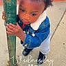 Deshawn is registered to the contest to win money with this photo: child, toddler, curly_hair, denim_jacket, black_shoes, sidewalk, pole, concrete, outdoor, daylight, curious, holding, street, casual_clothing, portrait, urban, young_child, expression, standing, person
