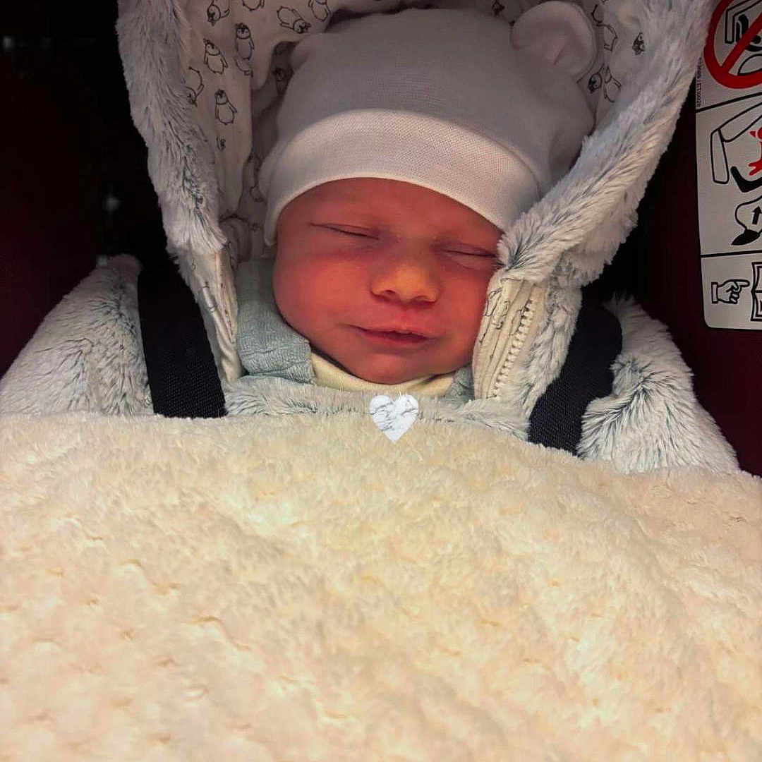 Mía participe au concours pour gagner de l'argent avec cette photo : baby, blanket, car_seat, child, child_seat, clothing, comfort, cozy, cute, face, fur, hat, headwear, infant, peaceful, portrait, rest, sleeping, soft, warm