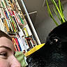 person, dog, black_dog, face, close_up, bookshelf, books, plant, green_plant, indoors, cozy, nose_to_nose, pet, animal, human, intimate, affection, portrait, home, sitting