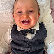 Lissandro a rejoint le concours — aidez-le/la à gagner de superbes lots ! baby, blanket, bow_tie, cheerful, child, clothing, cute, face, happy, indoor, infant, person, portrait, sitting, smiling, soft_texture, toy, vest, white_shirt, young_child