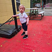 Nicolas joined the competition — help win amazing prizes! toddler, child, outdoor, basketball_hoop, pole, red_floor, yellow_wall, picnic_table, sneakers, bib, shorts, shirt, curious, standing, fence, trees, playground, summer, daytime, person