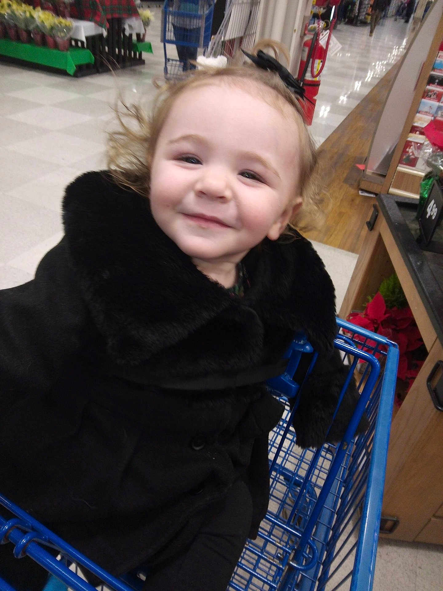 Jade is registered to the contest to win money with this photo: toddler, child, shopping_cart, black_coat, smile, indoor, store, aisle, holiday_decorations, person, curly_hair, happy, shopping, retail, cart, clothing, face, cute, winter_wear, young_child