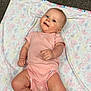 baby, infant, pink_onesie, blanket, floral_pattern, carpet, lying_down, smiling, child, cute, indoors, soft_lighting, happy, skin, face, hands, feet, head, person, portrait