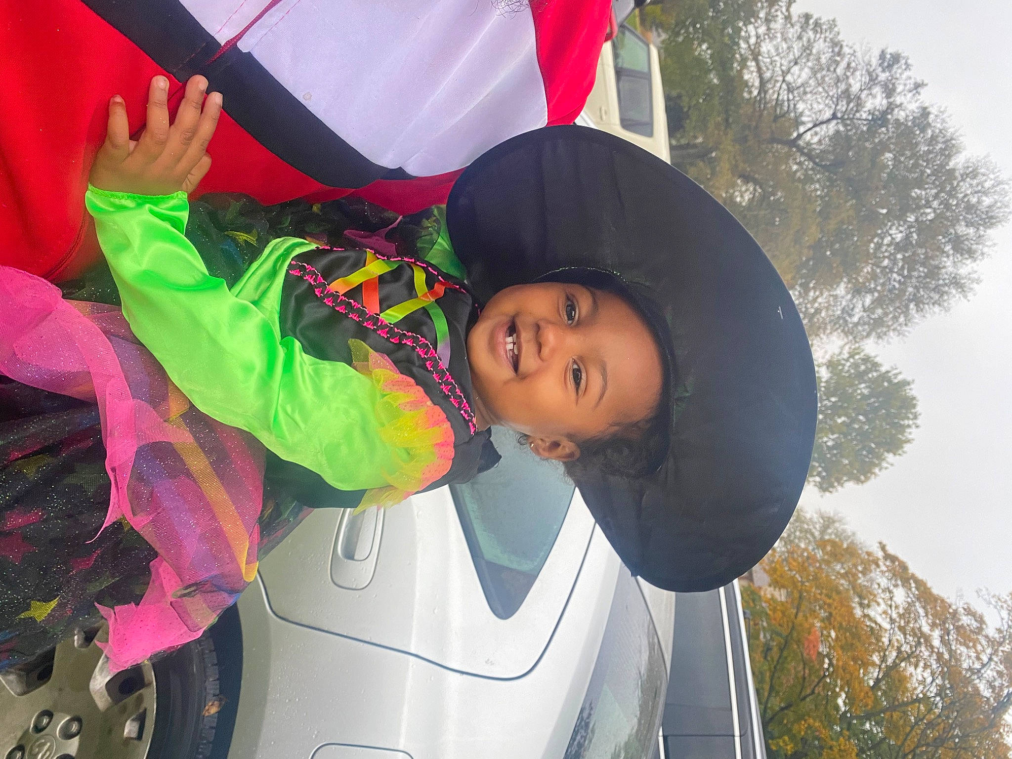 Peyton is registered to the contest to win money with this photo: alloy_wheel, automotive_lighting, automotive_tire, bumper, fender, fun, hat, headgear, hood, hubcap, joy, leisure, person, pink, red, smile, tire, tree, trunk, vehicle_door