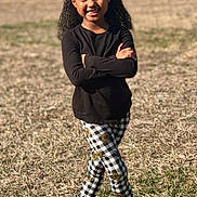 Peyton Carter joined the competition — help win amazing prizes! child, girl, smiling, outdoor, grass, sunlight, black_shirt, checkered_pants, sunflower_pattern, crocs, mismatched_socks, curly_hair, hair_bun, beads, standing, portrait, happy, playful_pose, casual_clothing, nature